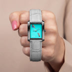 Laphont Bloc Cloudling — Held in a closed fist against a soft beige backdrop, the turquoise dial and the full length of the grey croc-embossed strap in view, a limited edition bespoke timepiece by IFL Watches